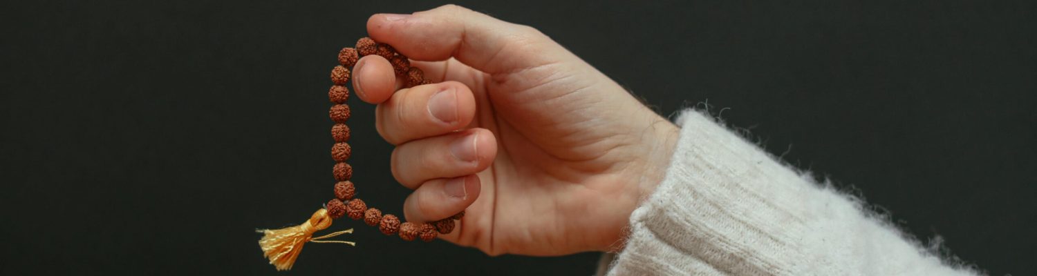 A close-up of a hand holding a beaded bracelet against a dark background.